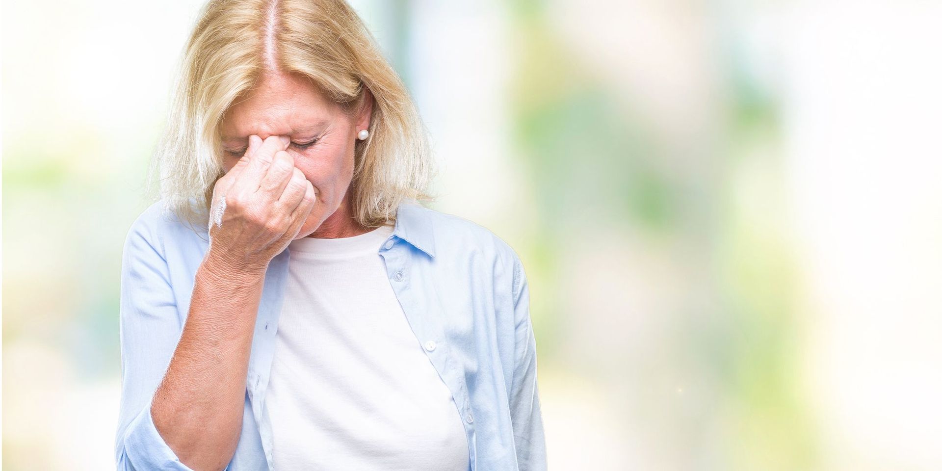 Eine blonde Frau die sich schmerzerfüllt an die Stirn fässt.